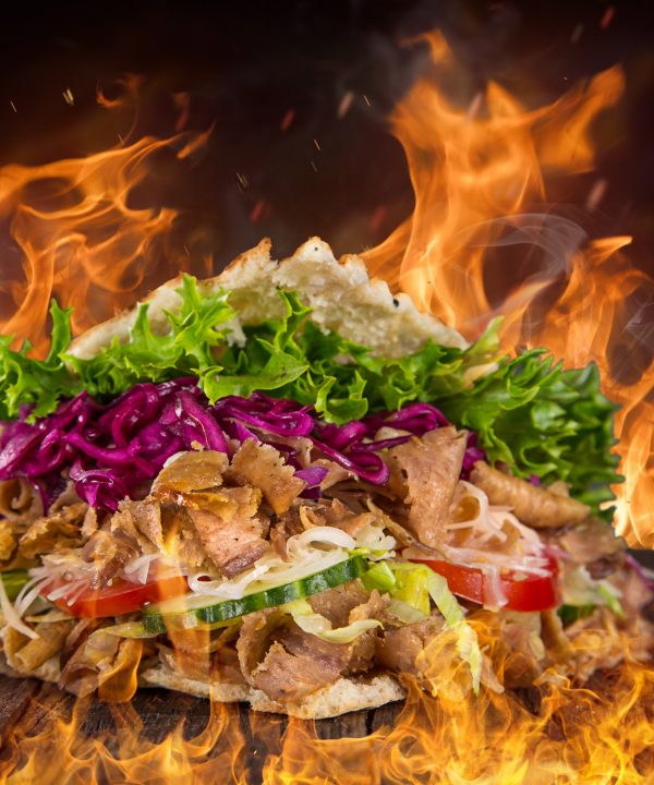 close up of kebab sandwich on wooden background with fire flames.